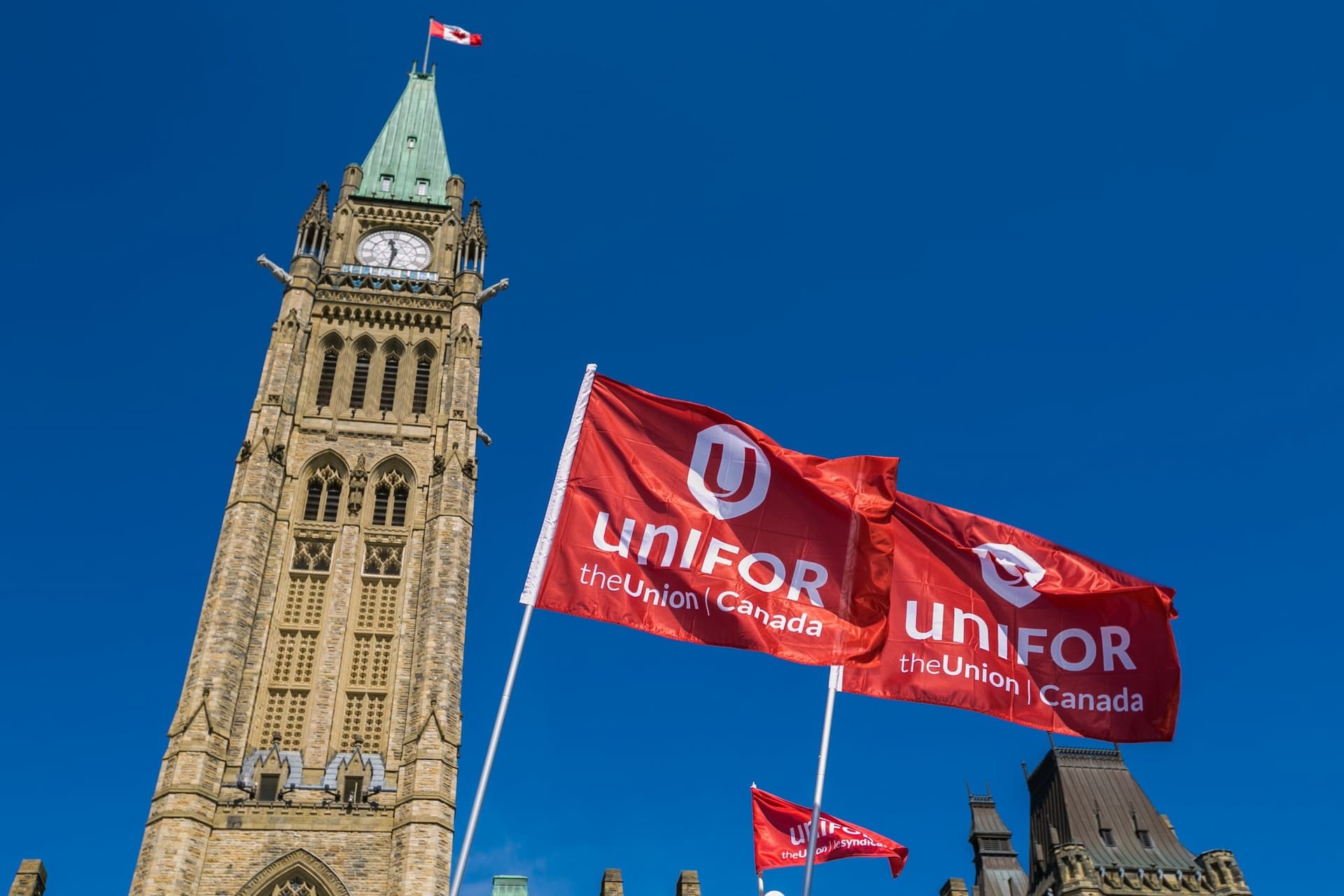 Unifor union flags flying in front of Parliament Hill Peace Tower in Ottawa, Canada
