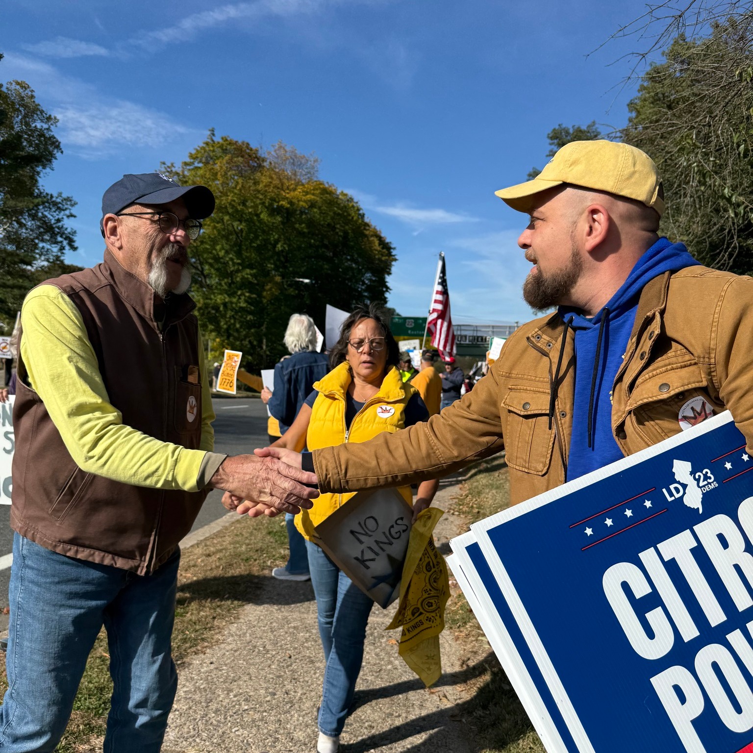 State assembly candidate Guy Citron shakes hands with a voter at a community rally in New Jersey’s 23rd Legislative District, holding campaign signage and engaging residents face to face.