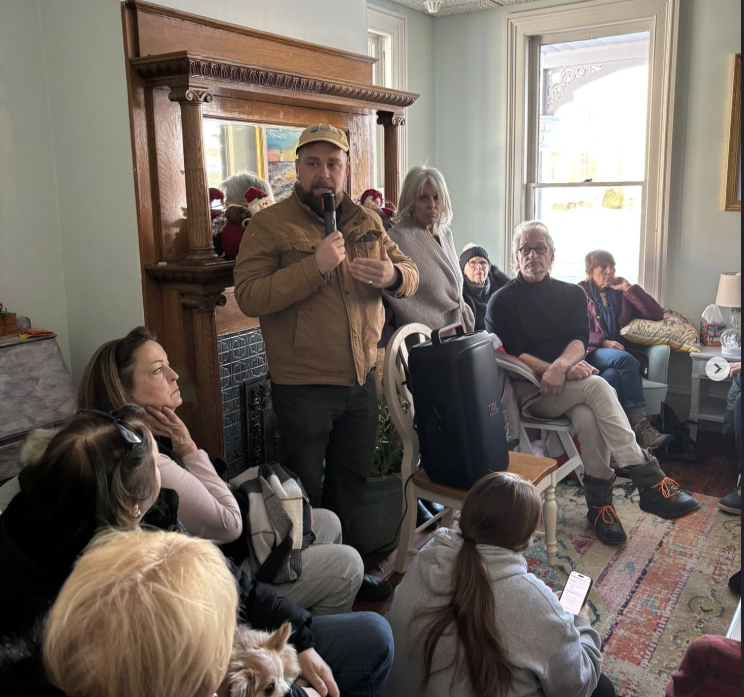 New Jersey state assembly candidate speaks to residents at a small indoor community meeting, holding a microphone and engaging voters in a living room setting.