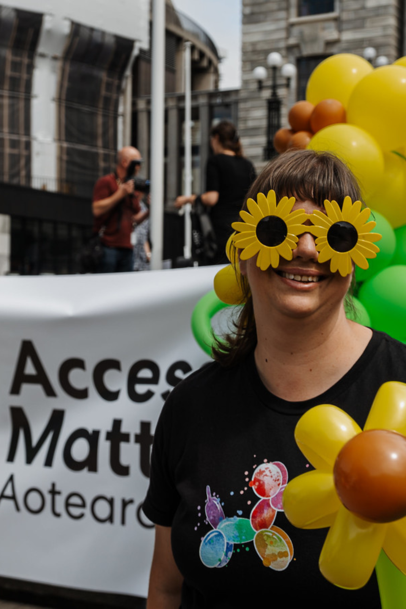 Sunflower balloon lady with Access Matters banner in front of NZ Parliament buildings crop