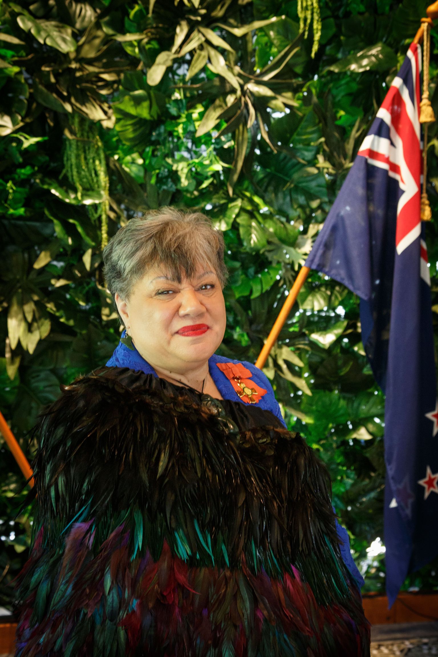 Chrissie Cowan wearing korowai  ONZM medal with NZ flag in background %28sml%29