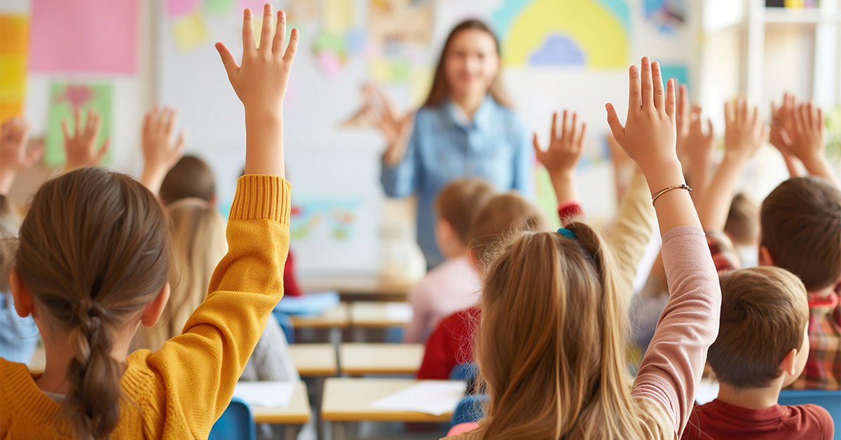Classroom of children with raised hands and teacher at front