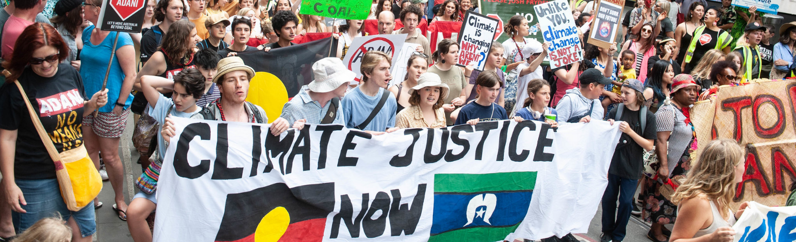 young people at a rally with a banner reading climate justice now