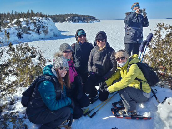 A group of people in winter clothes and snowshoes stand on top of snowy cliffs at The Grotto at Bruce Peninsula National Park