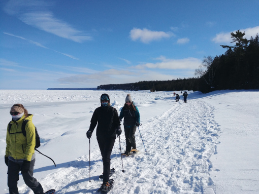 A group snowshoe across snowy ice in a line at The Grotto in Bruce Peninsula National Park