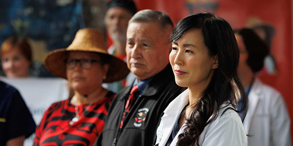 Side close-up of Dr. Melissa Lem in a white lab coat alongside First Nations leaders