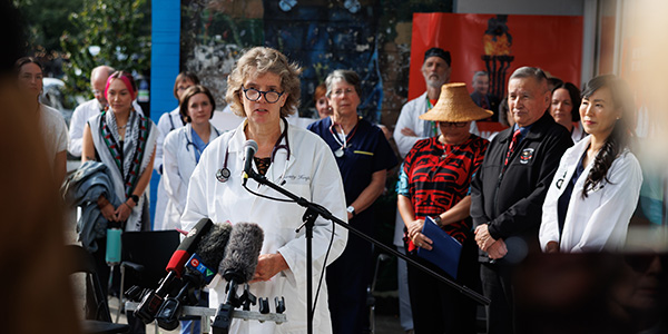 Dr. Ulrike Meyer speaking into a microphone with physicians and First Nations leaders behind