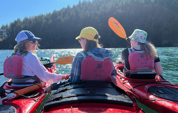 Photo of three CAPE staff kayaking from behind, with background of trees