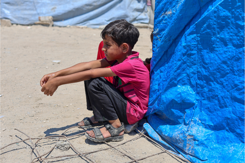 A Palestinian boy sits near his family's tent in Gaza. Photo by DCIP. 
