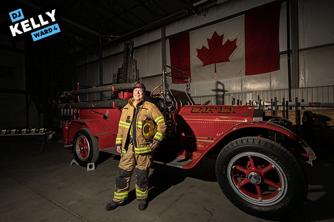 Img Alt: Cllr. DJ Kelly, without his beard, stands in front of a historic fire truck at the Calgary Fire Department's training centre as part of Fire Ops 101 on May 8, 2026. (Aryn Toombs / Ward 4)