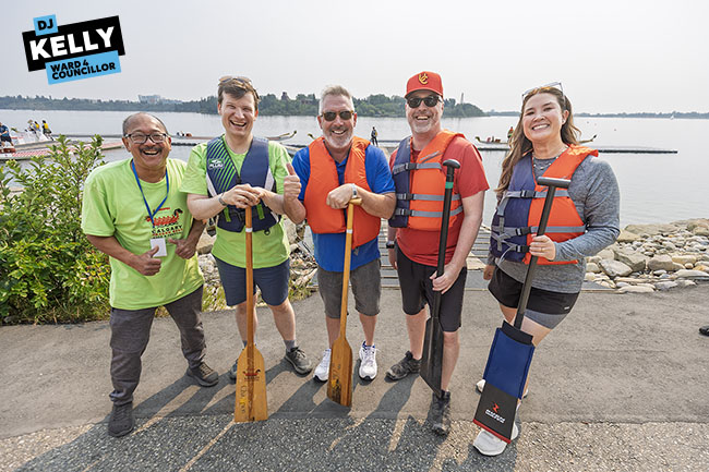 Img Alt: Danny Ng, Chair of the Calgary Dragon Boat Festival Society, left, Mayor Jeromy Farkas, Ward 13 Councillor Dan McLean, Ward 4 Councillor D.J. Kelly, and Ward 1 Councillor Kim Tyers pose for a photo ahead of the festival's charity race for Meals on Wheels at North Glenmore Park on Aug. 9, 2026. (Aryn Toombs / Ward 4)