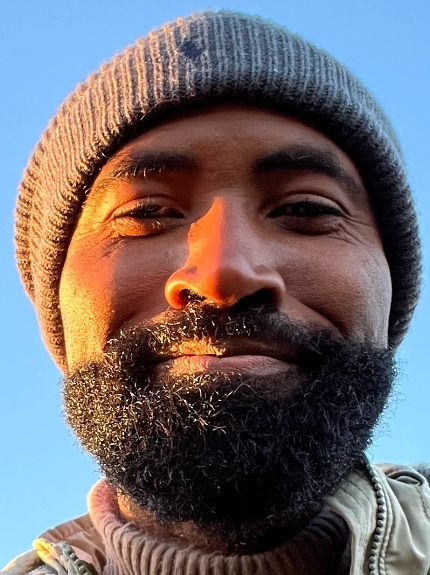A smiling person with a beard and a hat