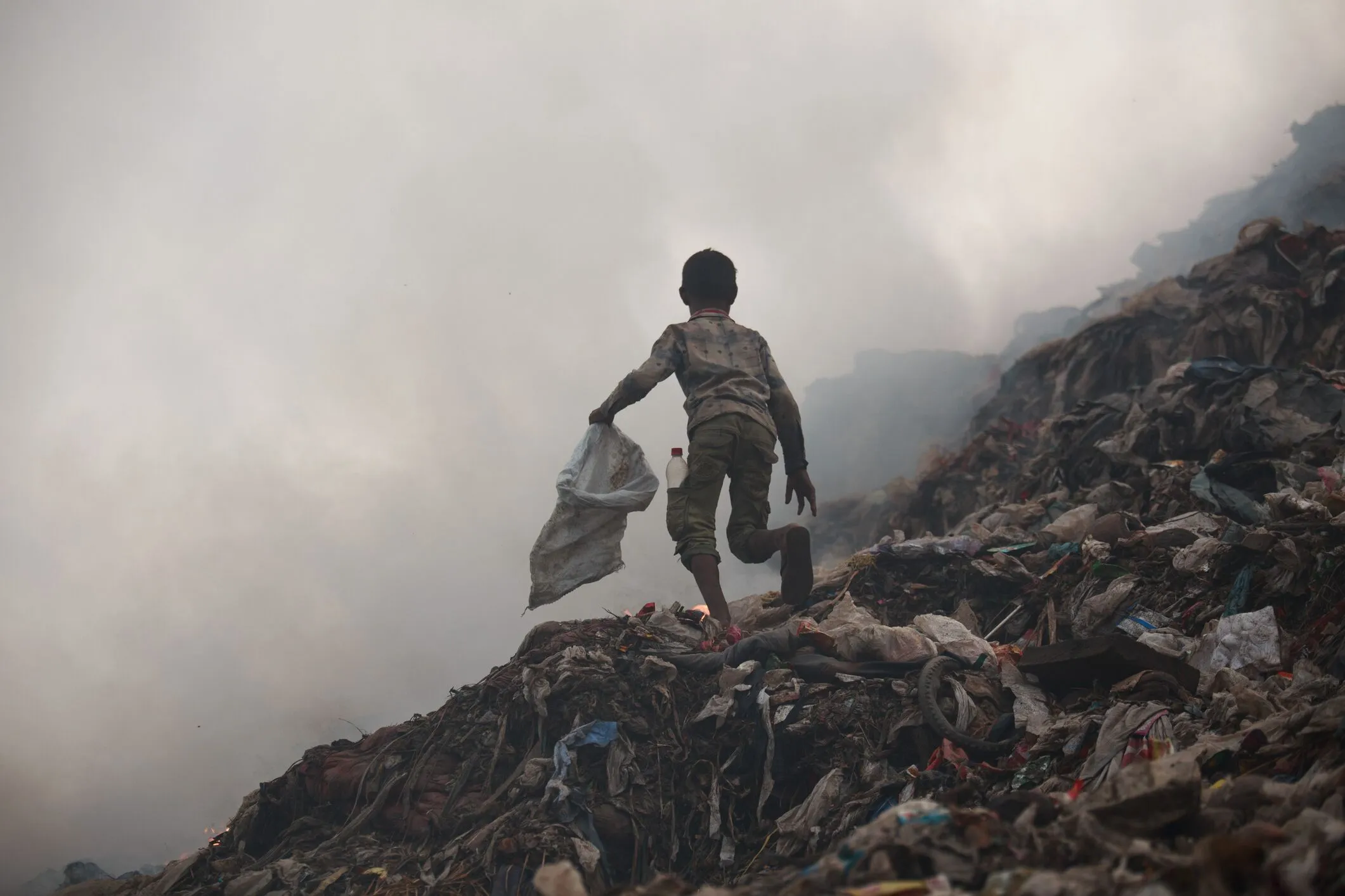 small child running through an overflowing
dumpground with a bag