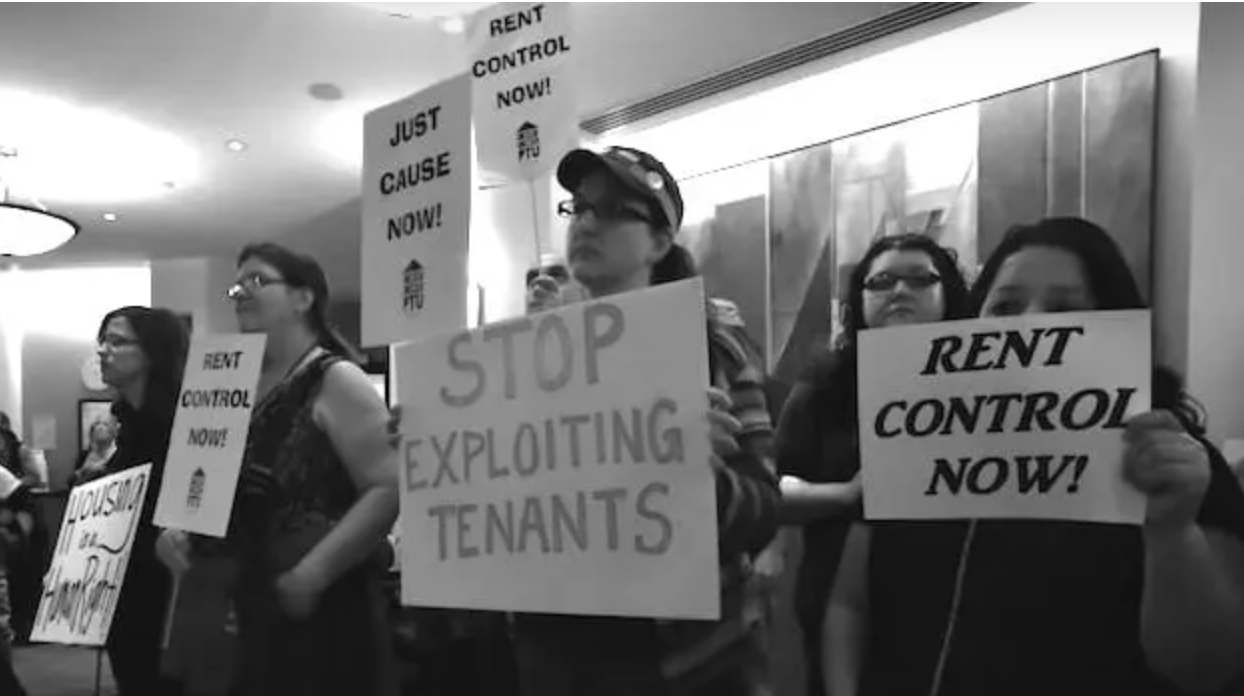People holding signs: Rent Control Now! Housing as a Human Right. Stop Exploiting Tenants. Just Cause Now!