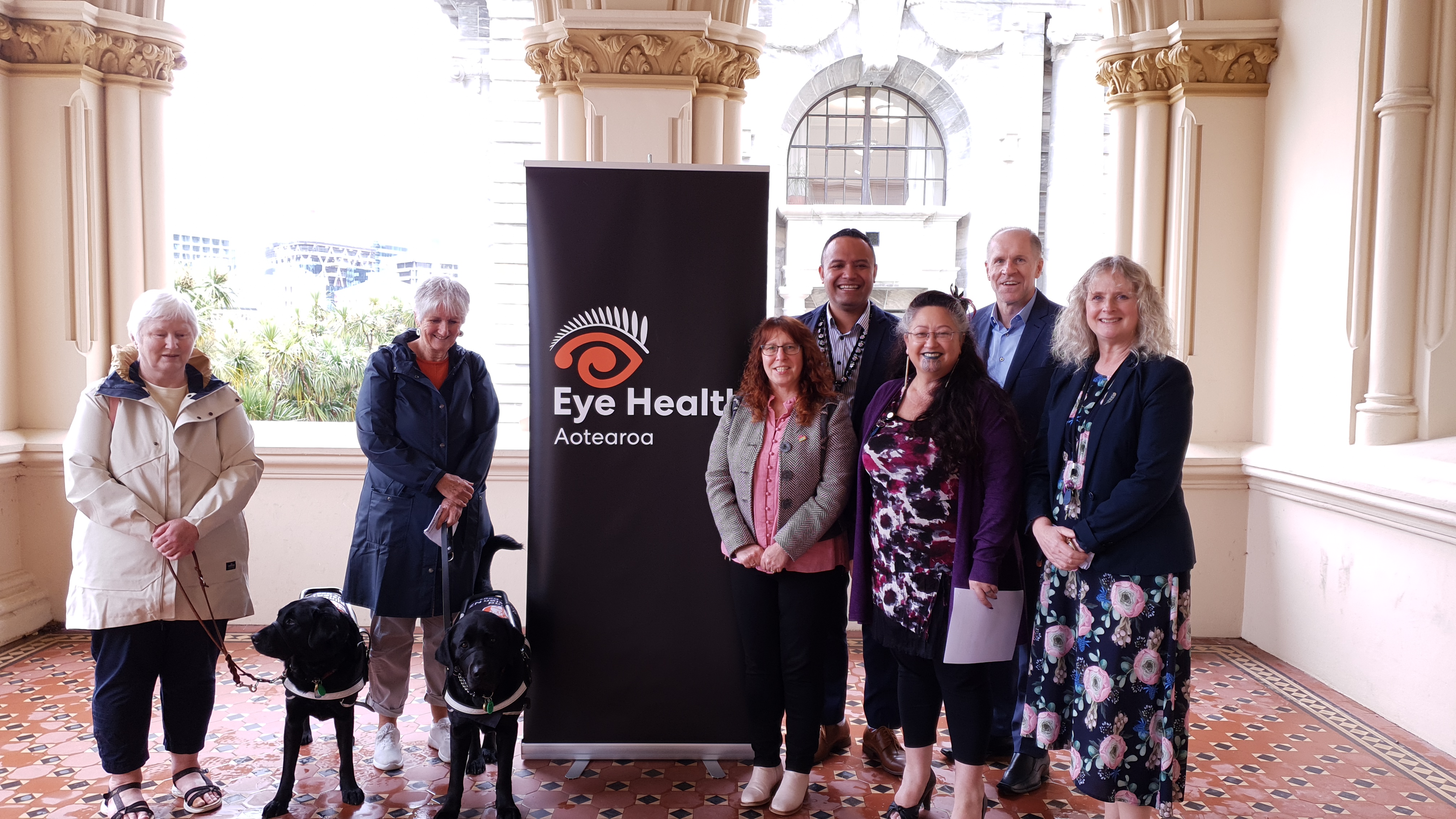 EHA representatives and NZ politicians with framed petition standing next to Eye Health Aotearoa banner.