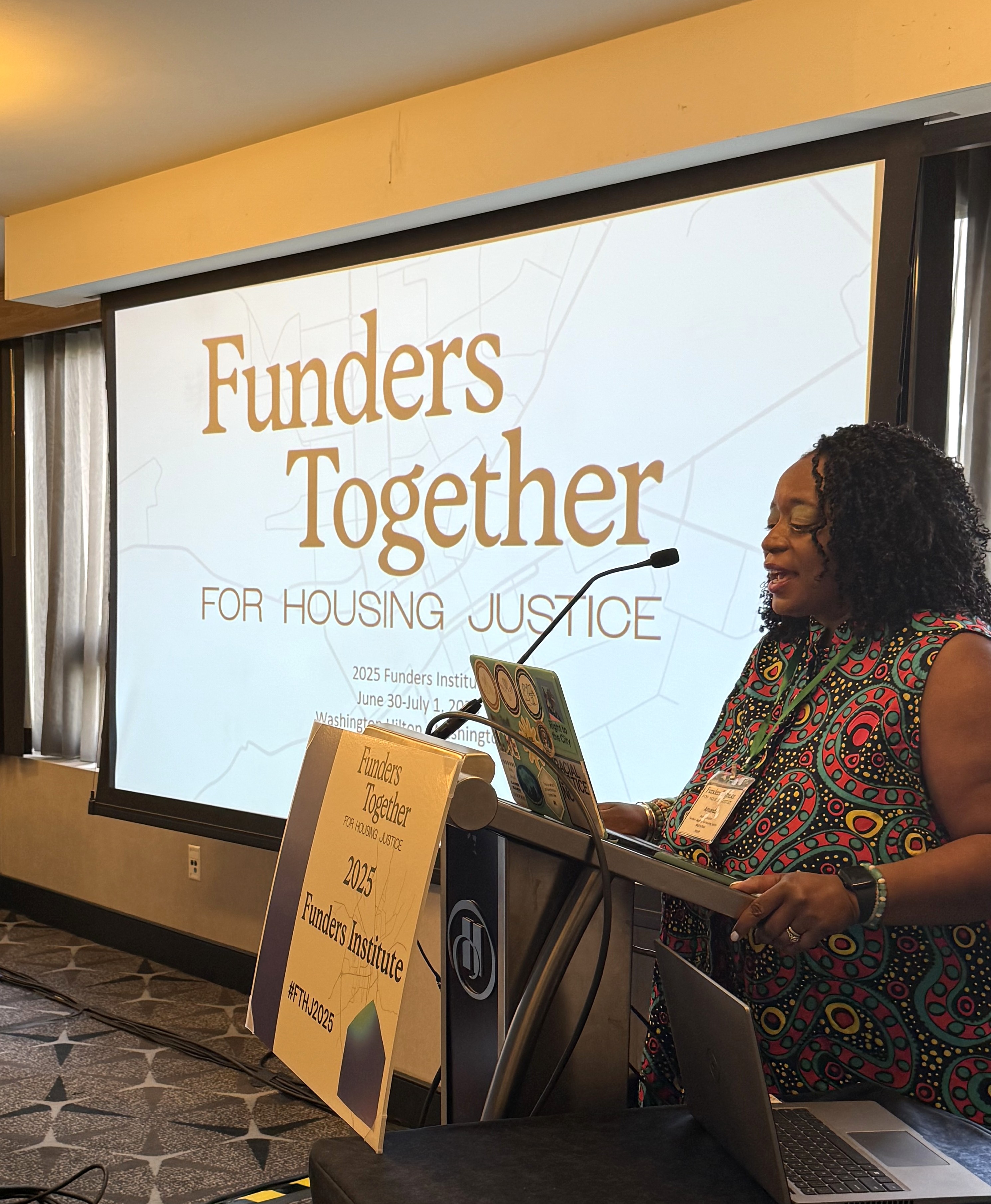 A black woman stands at a podium in front of a screen that reads Funders Together for Housing Justice