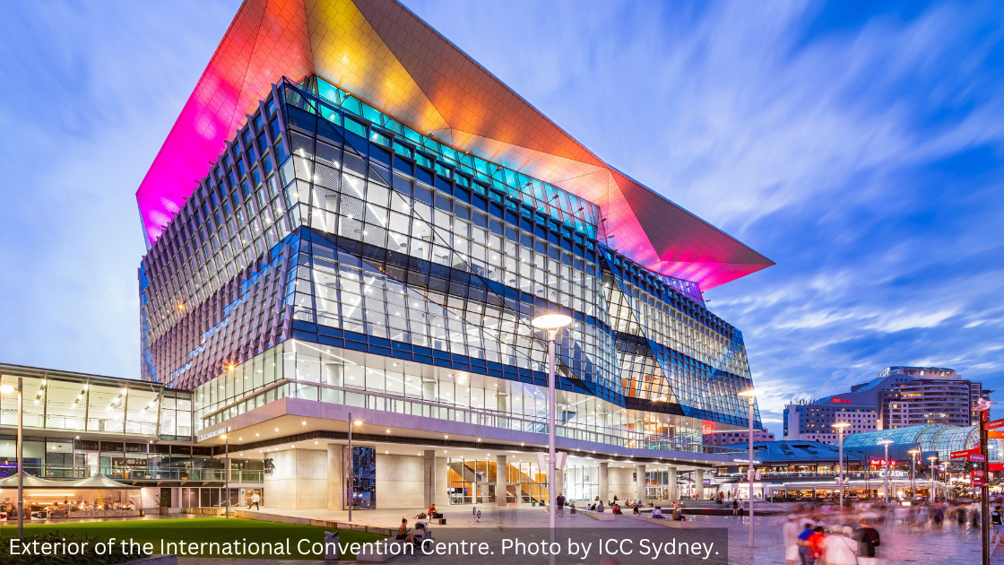Exterior shot of the International Convention Centre Sydney lit up with colourful lights against a blue sky.