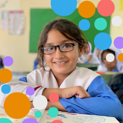 Young girl wearing glasses smiles, colorful
dots in the corner. 
