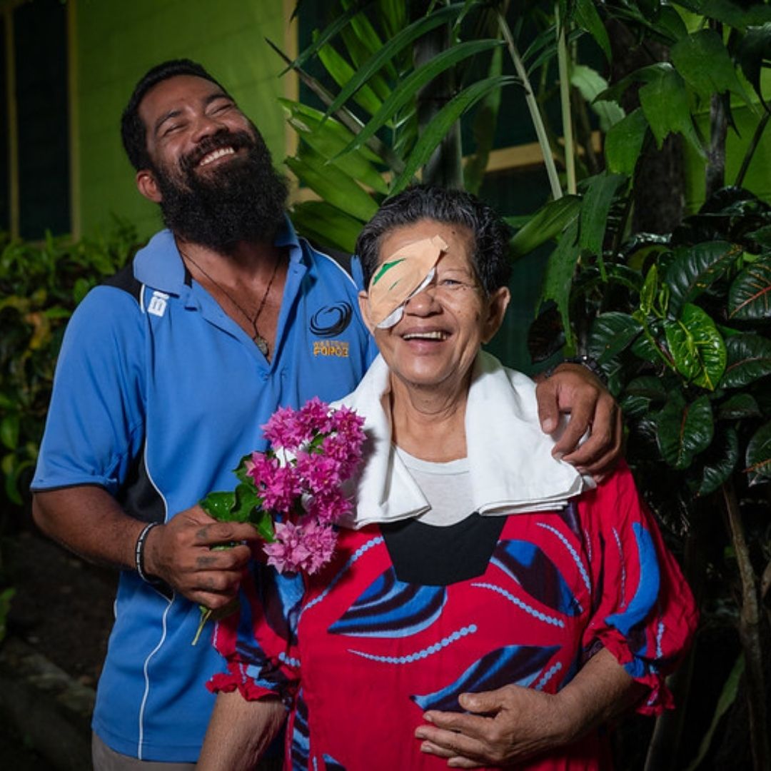 Two young children sit at a desk at school.
They are smiling and wearing heart shaped glasses.