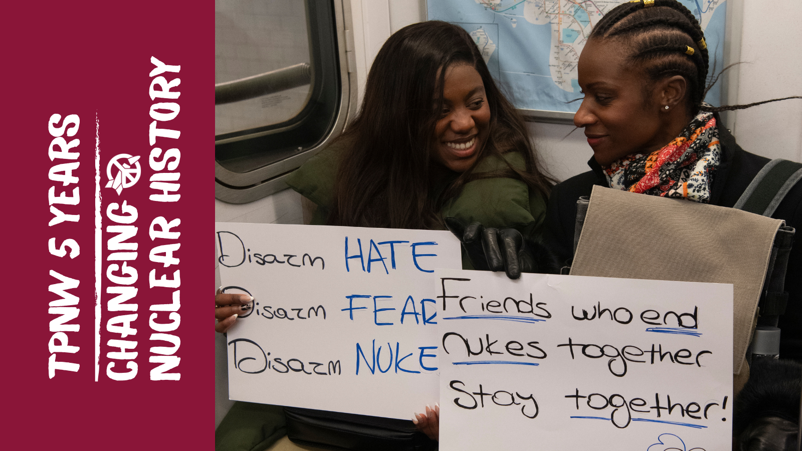 Two people sitting on subway with signs against nuclear weapons