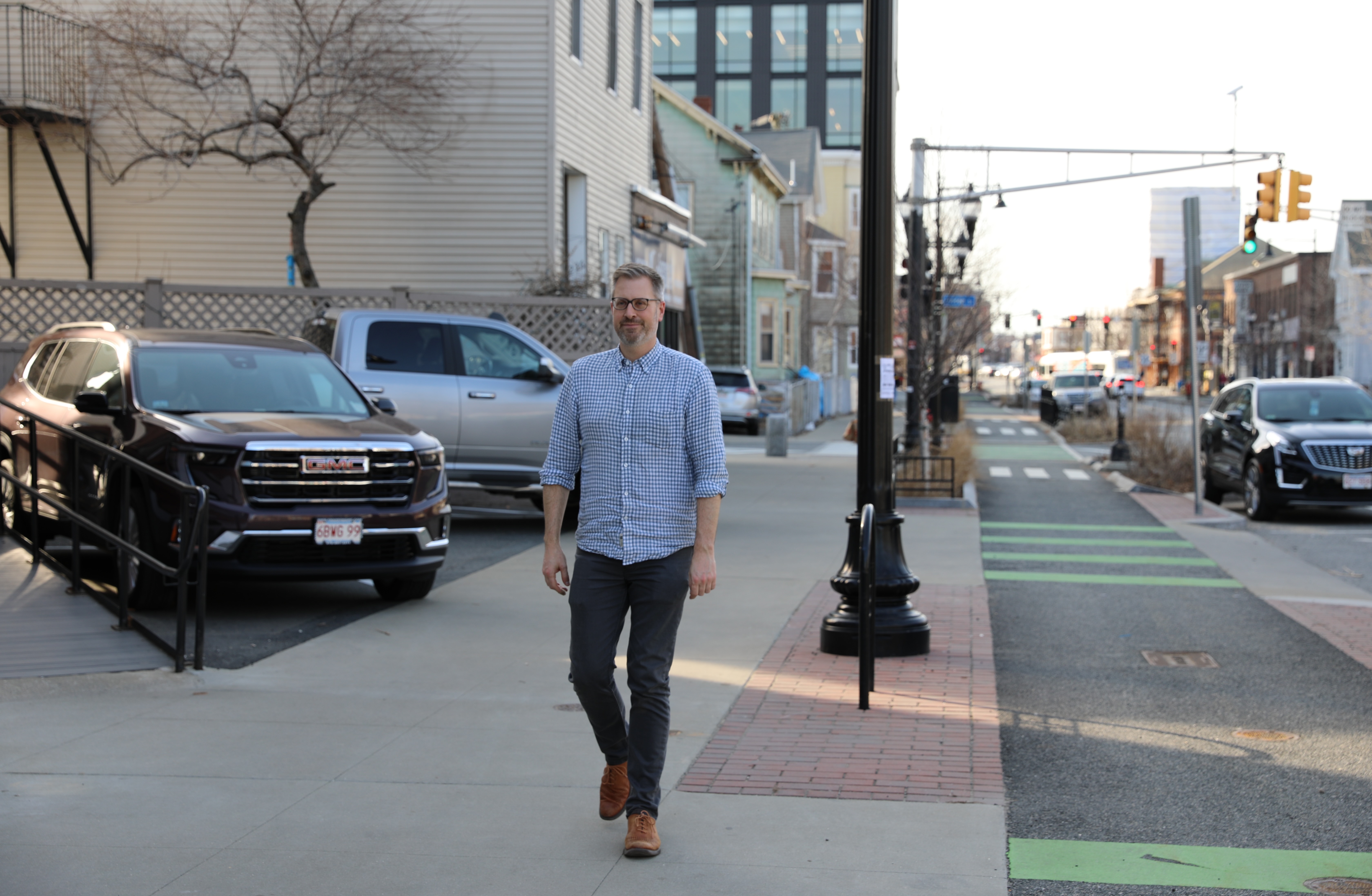 Jake walking on the sidewalk flanked by a raised bike path and a parking lot on either side