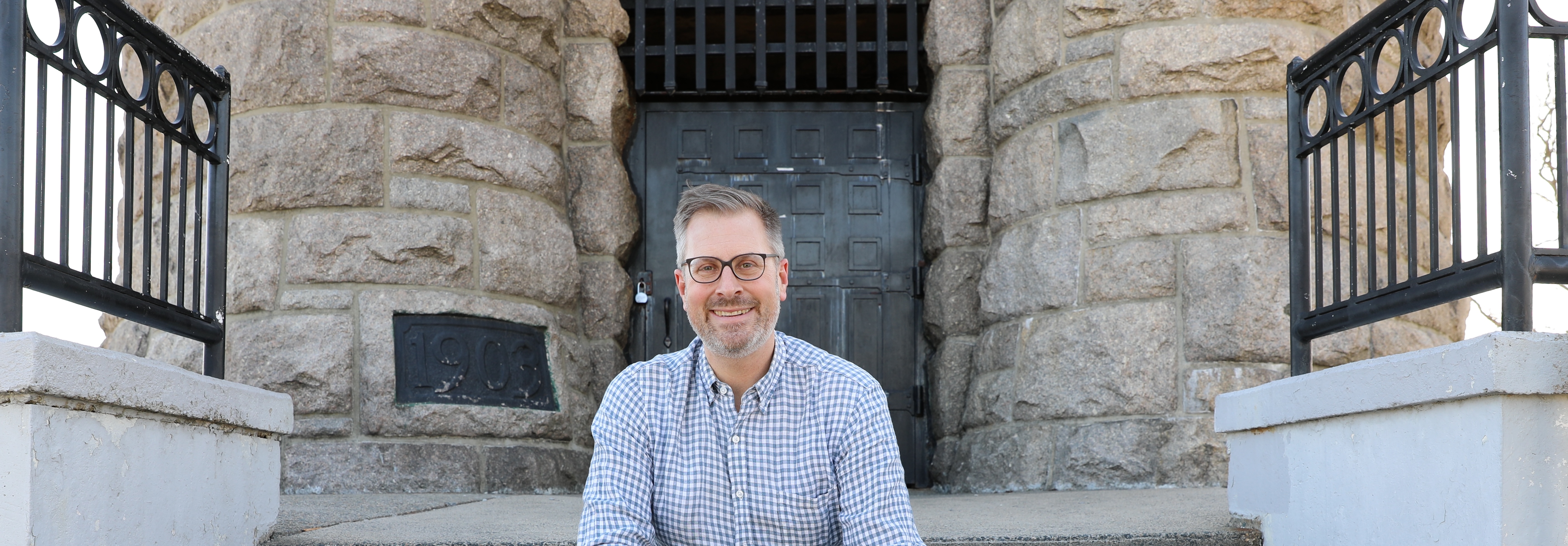 Jake smiling as he sits on some steps in front of a stone building