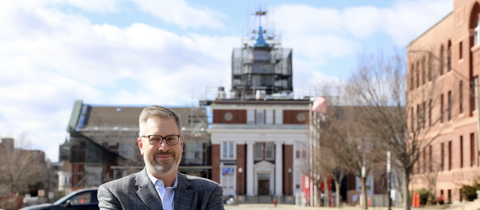 Jake poses in front of Somerville City Hall, which has scaffolding in the background.