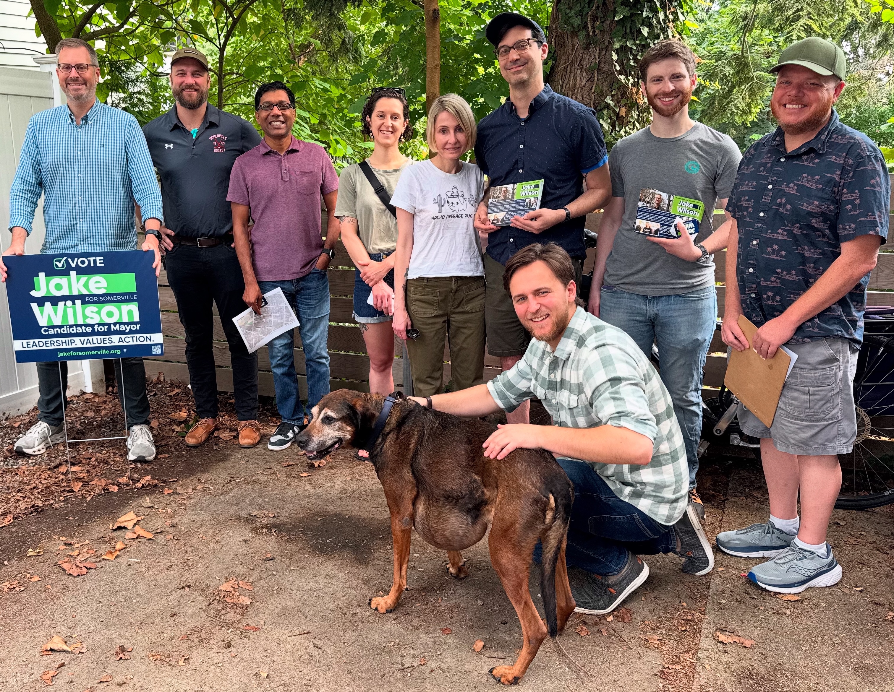 Jake and a group of people pose for a picture. In the foreground, a person poses with their dog.