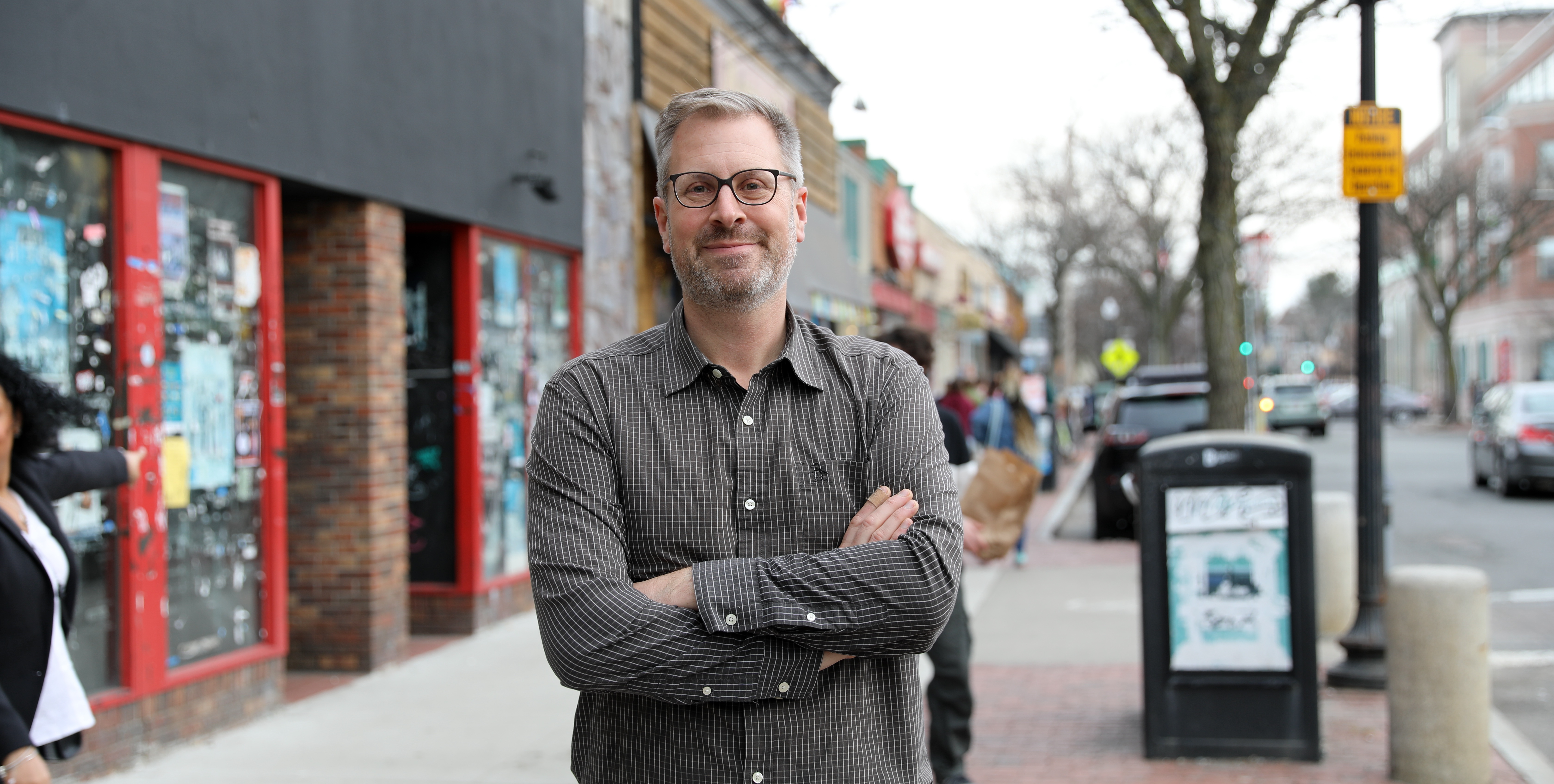 Jake Davis Headshot Jake poses in front of businesses in Davis Square on the sidewalk