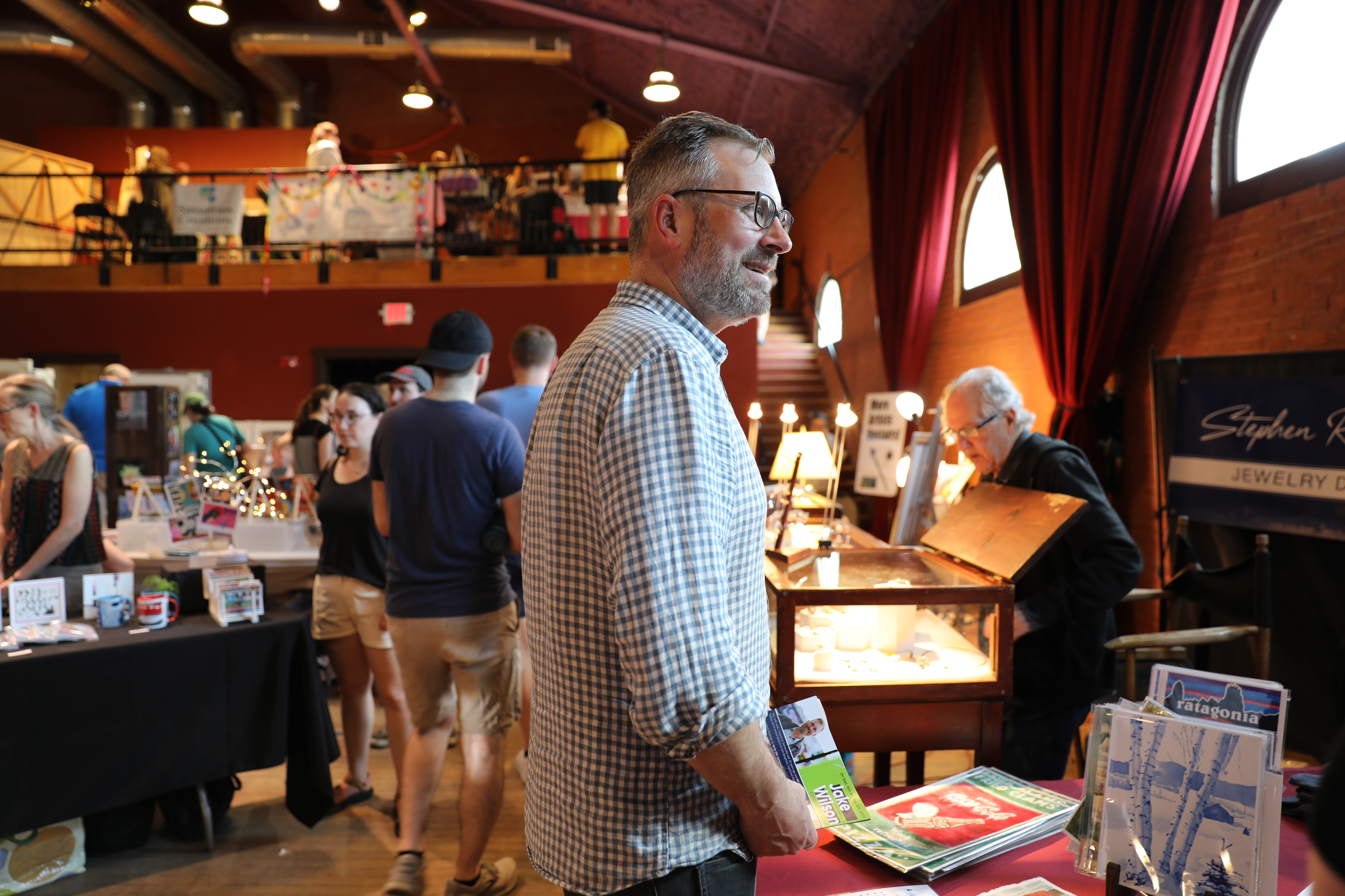 Jake stands near a table with a red table cloth and programmatic materials on it in a large room