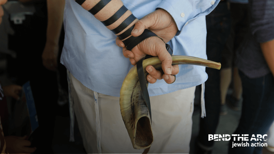 Bend the Arc: Jewish Action hand holding 
shofar with tefillin