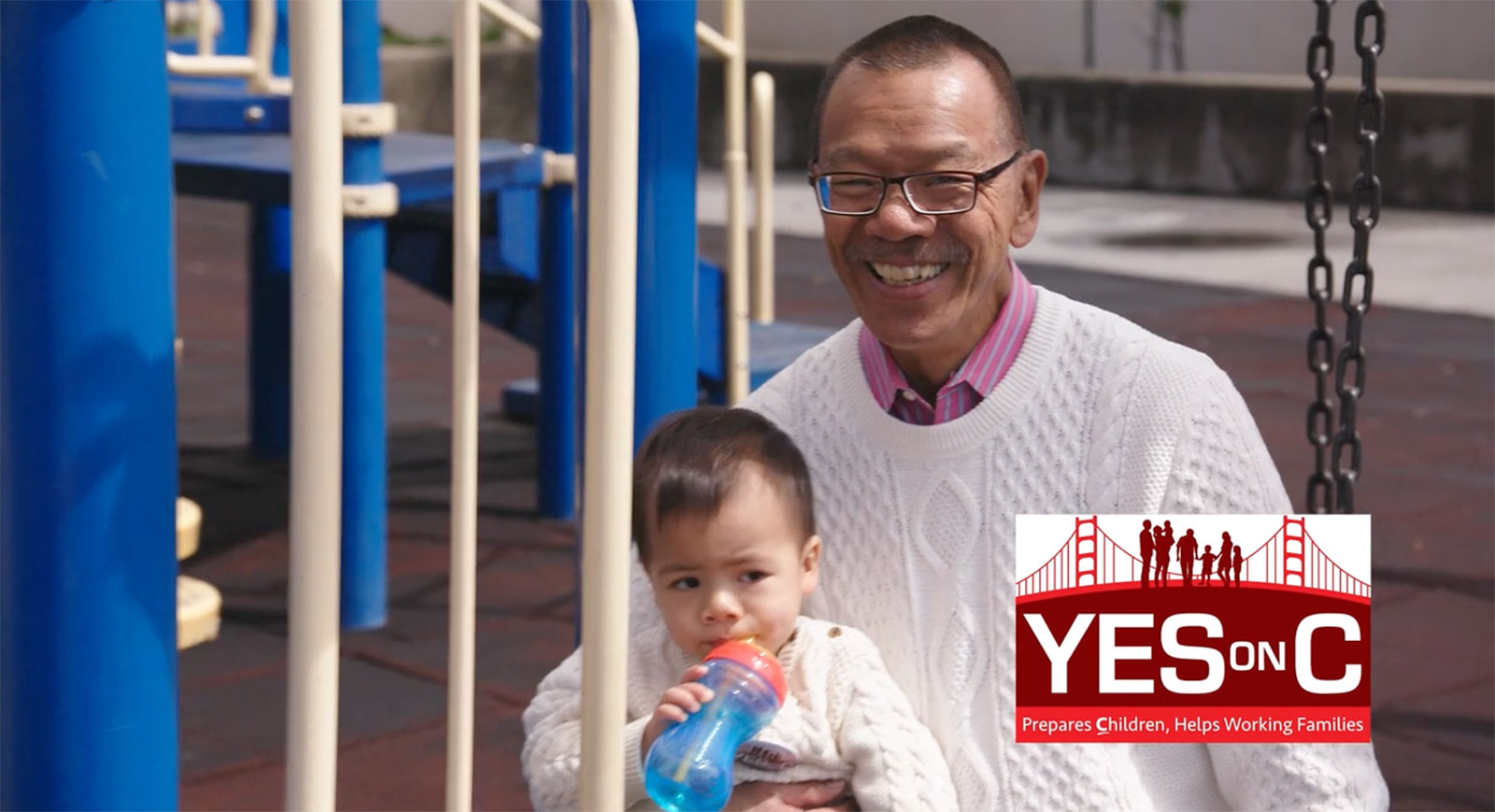 Supervisor Norman Yee smiling while holding a young child at a playground, promoting San Francisco Proposition C for childcare and early education.