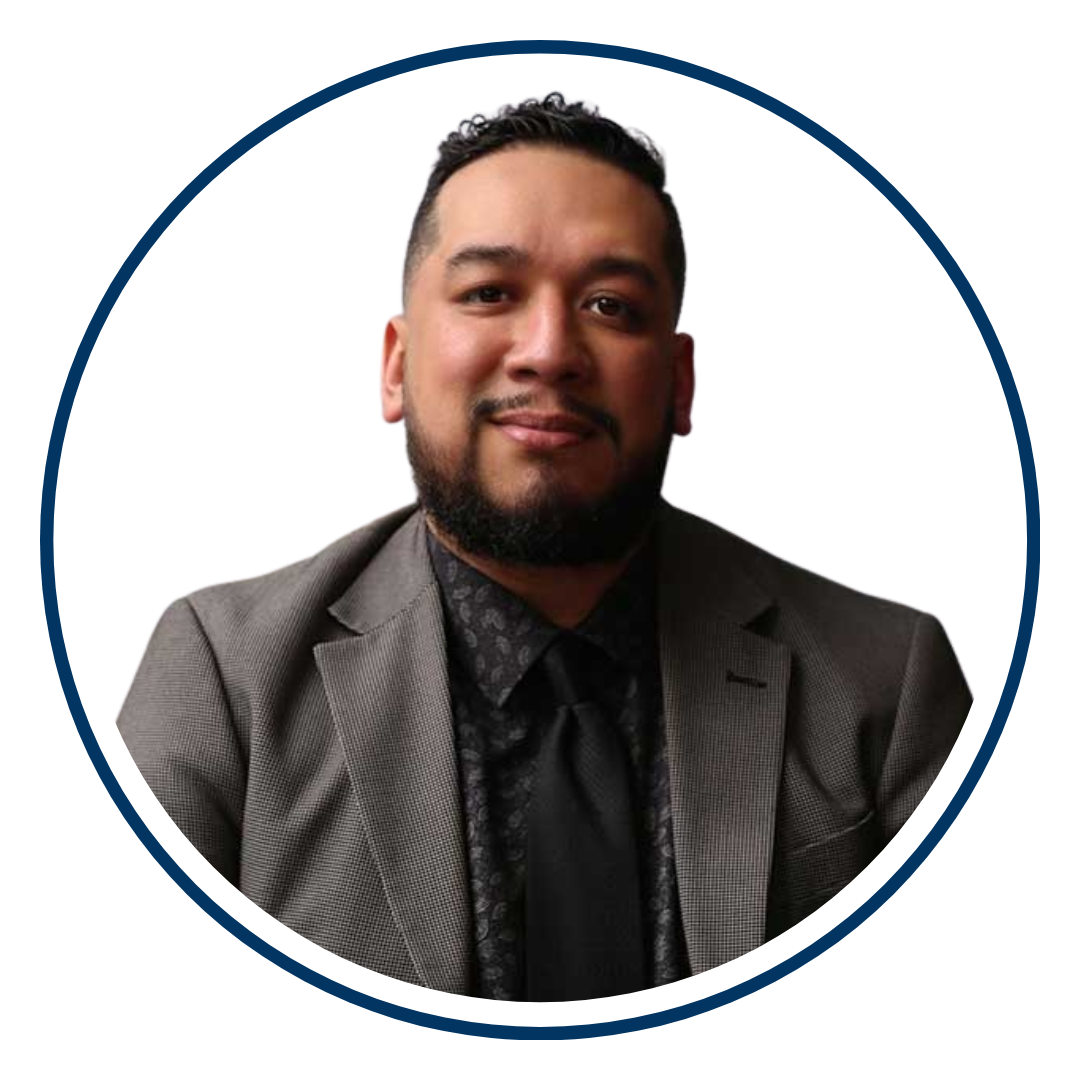 Latina male with dark hair and dark beard wearing a dark brown blazer and Black shirt