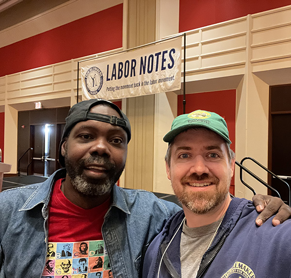 Photo of Will and Nate in front of a Banner that says Labor Notes. Nate is wearing a DC 37 hat.