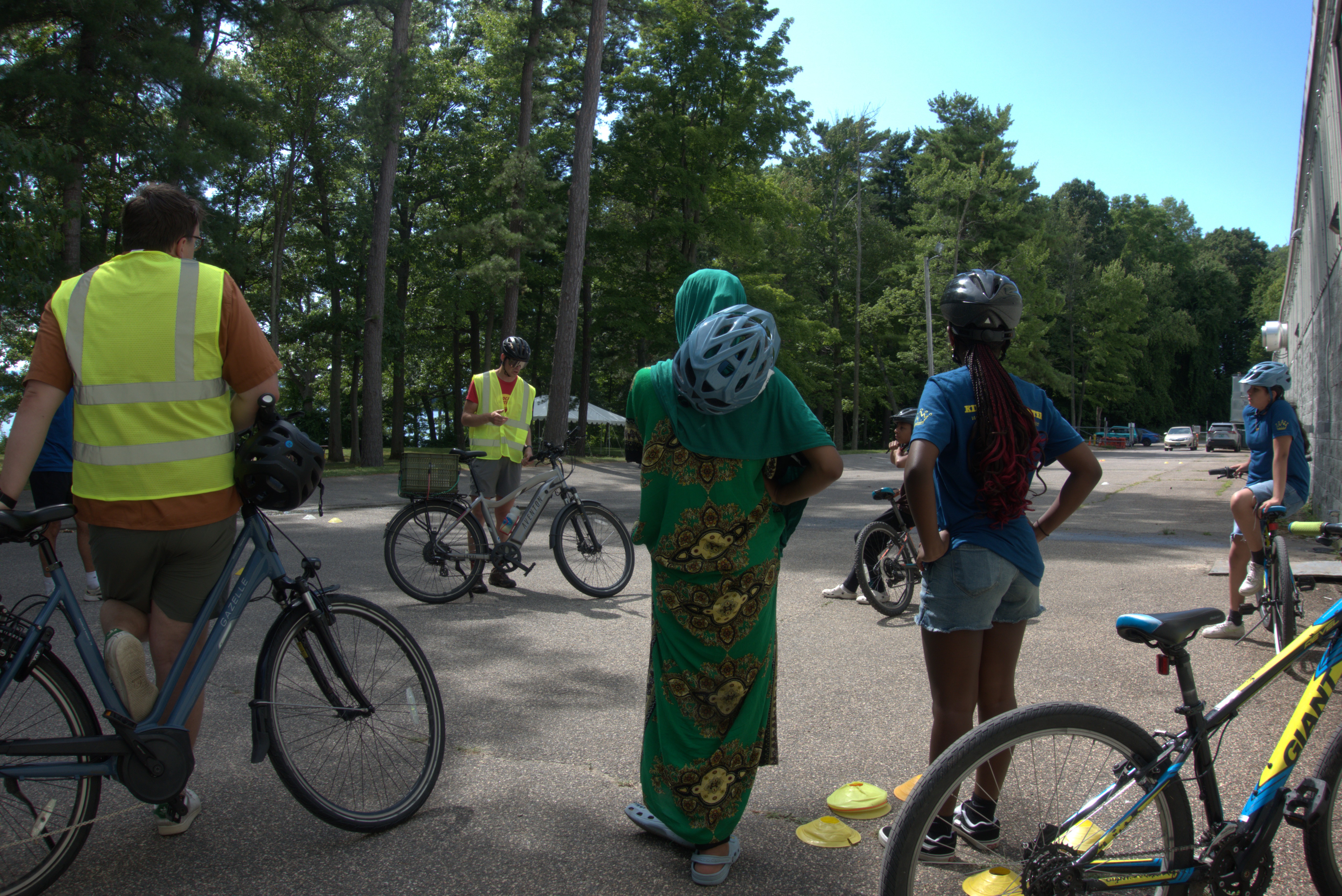 Daniel is standing with his bicycle and speaking to a group of 4 King Street Center kids who are all looking on wearing helmets and prepared to ride