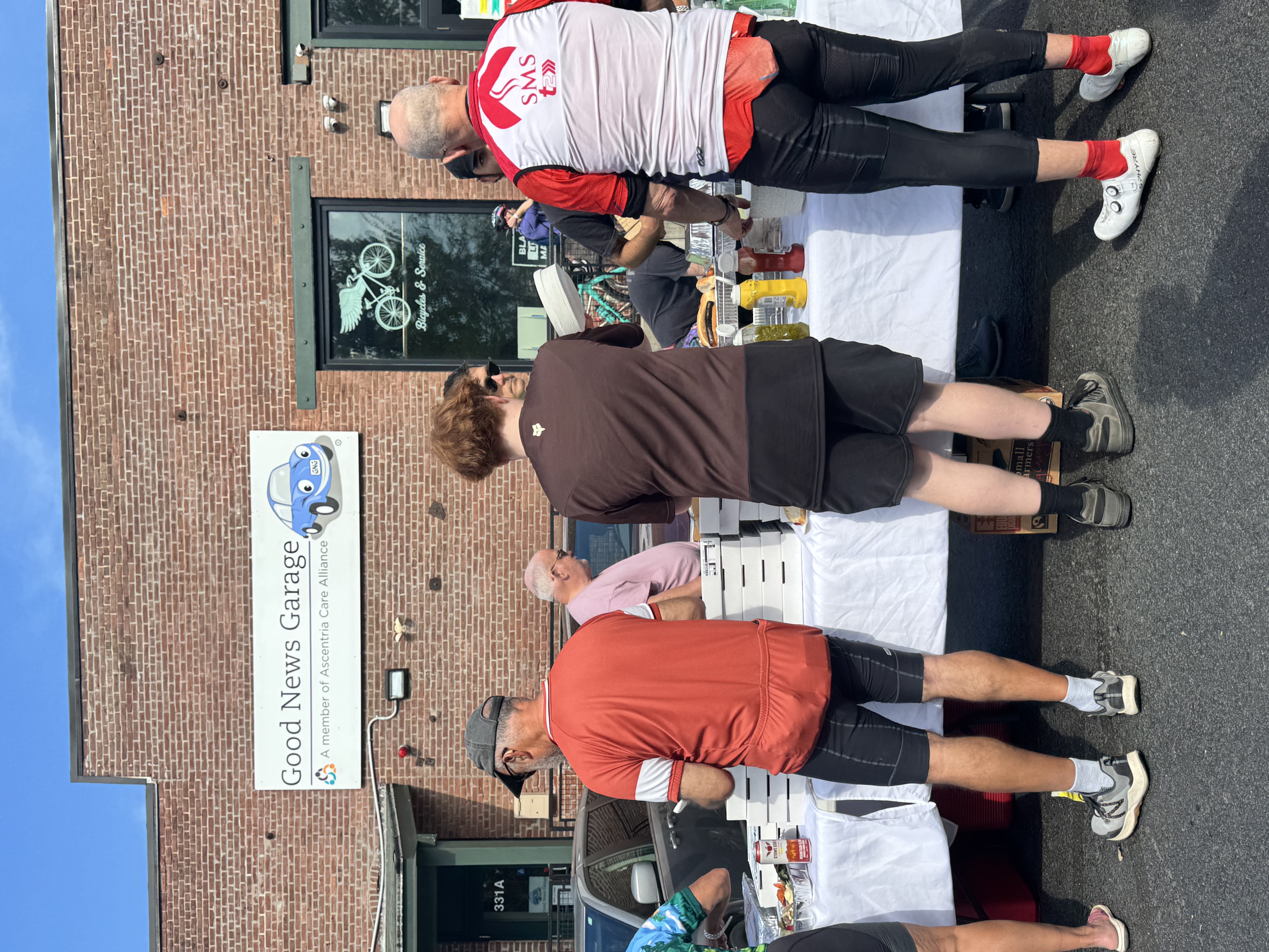 Riders picking up post-event pizza from a long table outside of Old Spokes Home