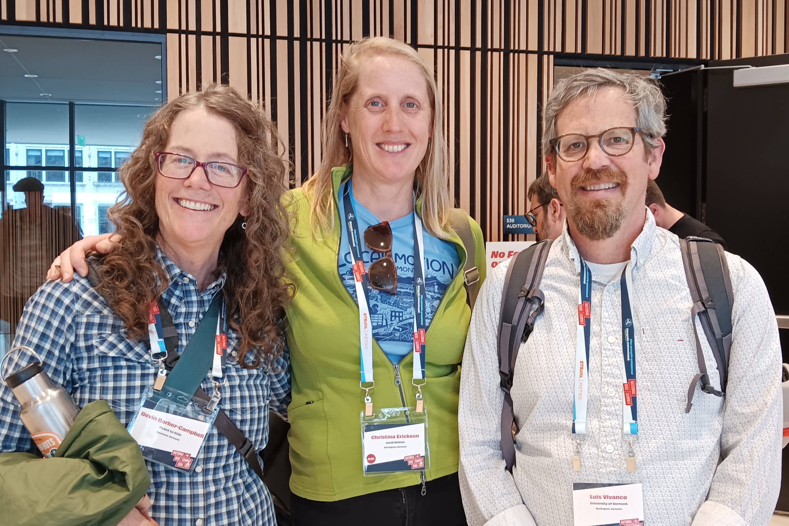 Bevin, Christina, and Luis stand together and smile in a busy hallway at the Bike Summit