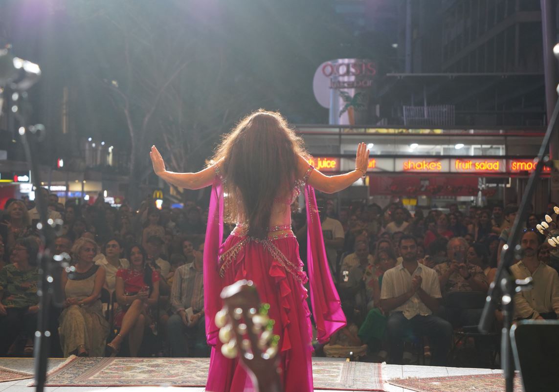 A dancer centre stage in front of a large crowd, dancing in a pink traditional outfit.