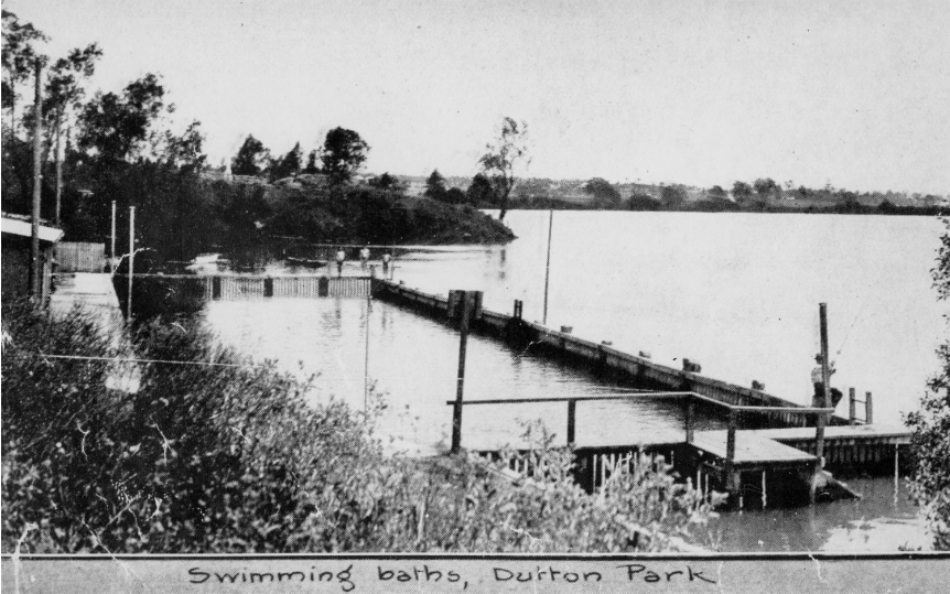 This image shows old swimming baths in the Brisbane river at Dutton Park in 1921. The baths are made of wood, and sit within the river itself. Nobody is currently swimming.