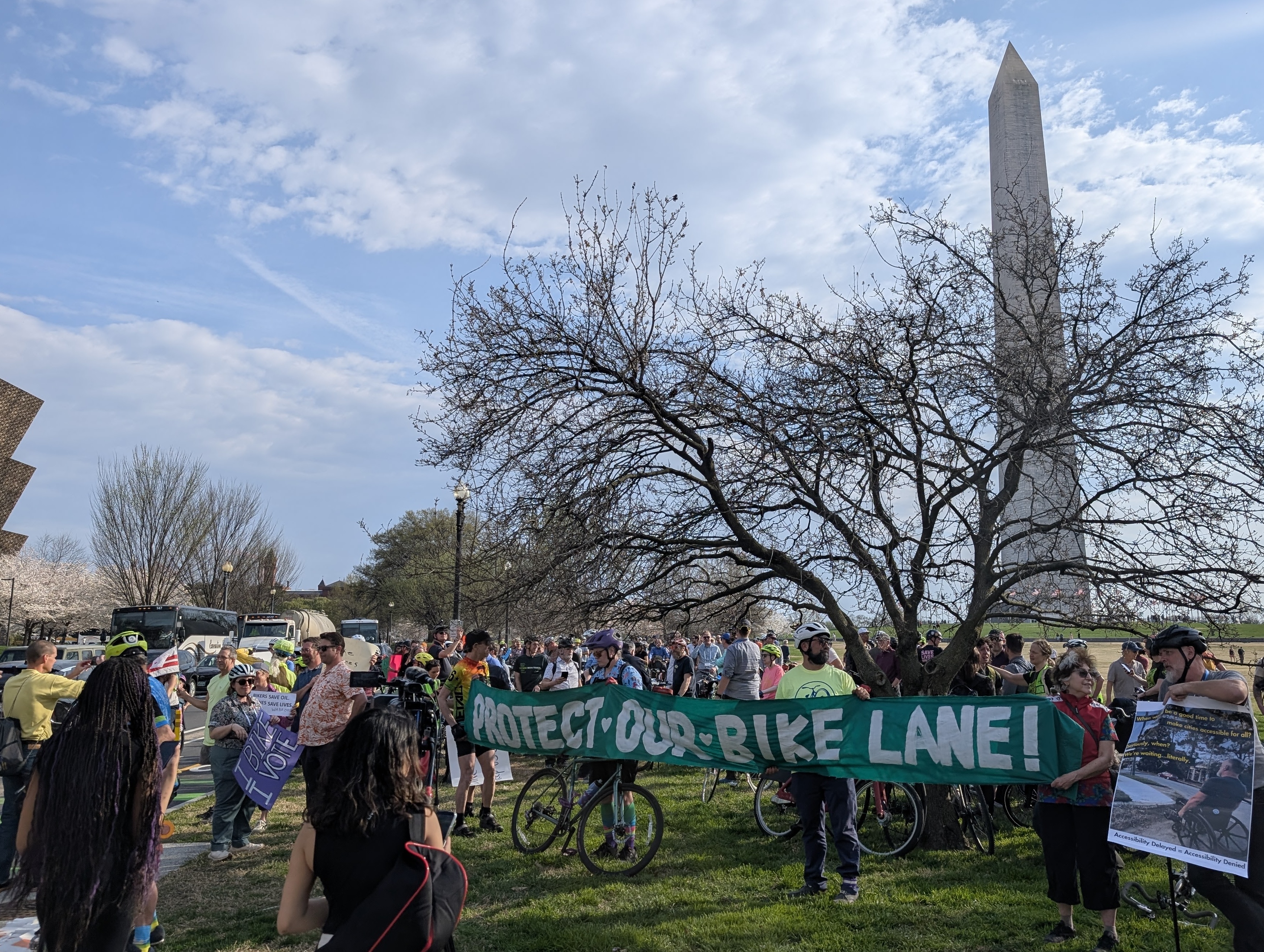 a group of people wearing bike helmets are gathered in a group; a few people are holding up a cloth sign that says \
