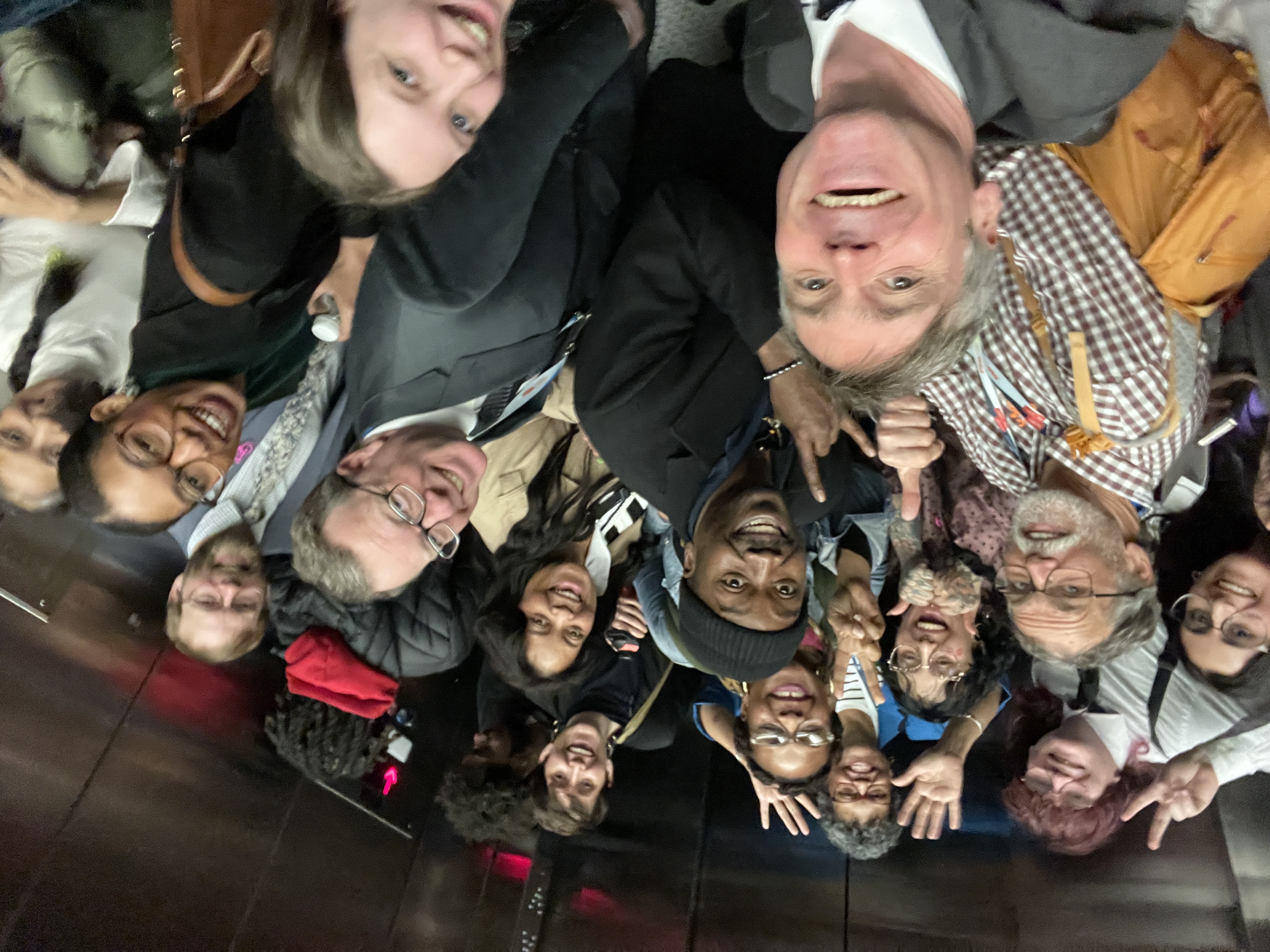 The MA delegation in an elevator, smiling for a group selfie. the group is around 20 people of diverse ages, races, and gender identities.