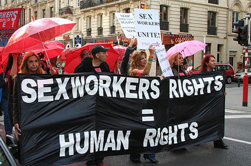 A photo from a march showing people holding red umbrellas and a large banner reading 'Sex worker rights = human rights'