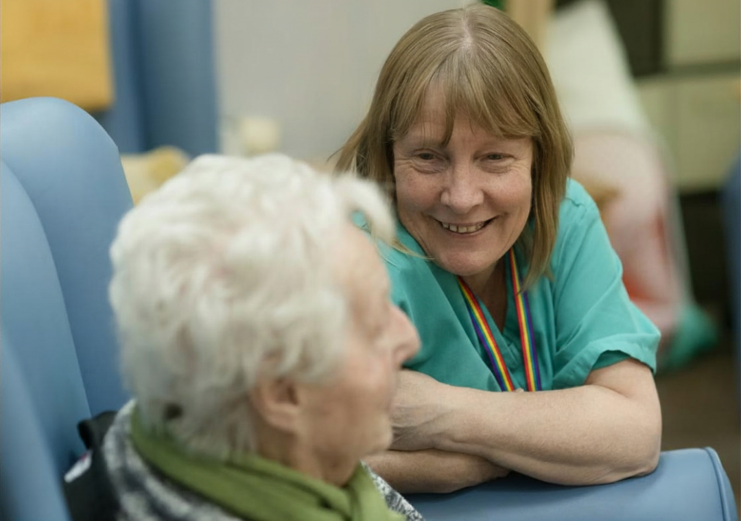 An aged care worker with a rainbow lanyard smiling at an older person