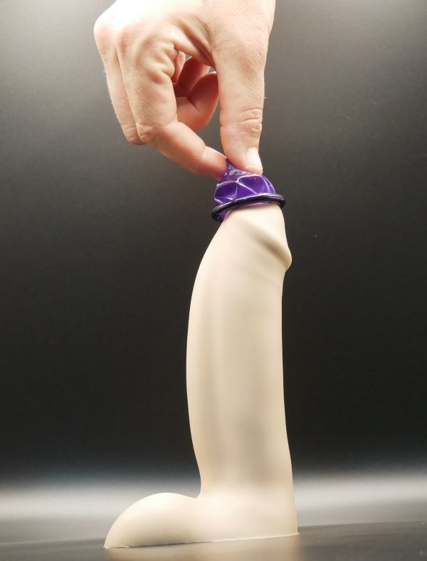 Image of a condom placed on top of a penis-shaped sex toy while a hand is squeezing the tip