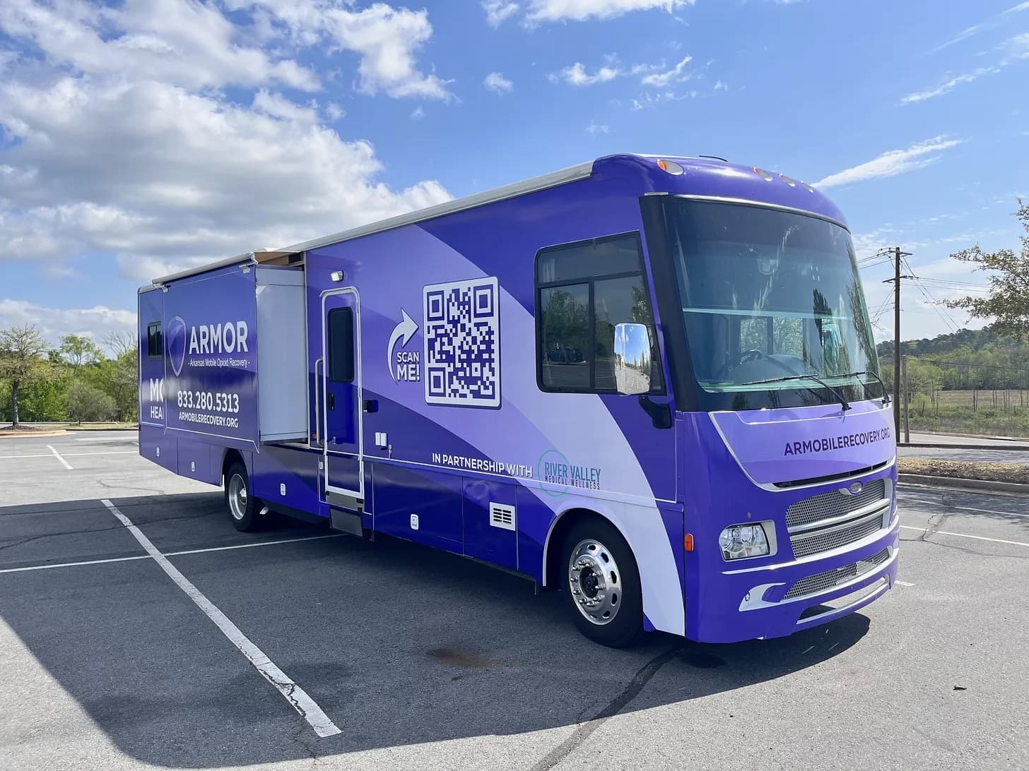 A large purple ARMOR mobile opioid recovery RV parked in a lot, with logos, QR code, and ‘armobilerecovery.org’ on the side.
