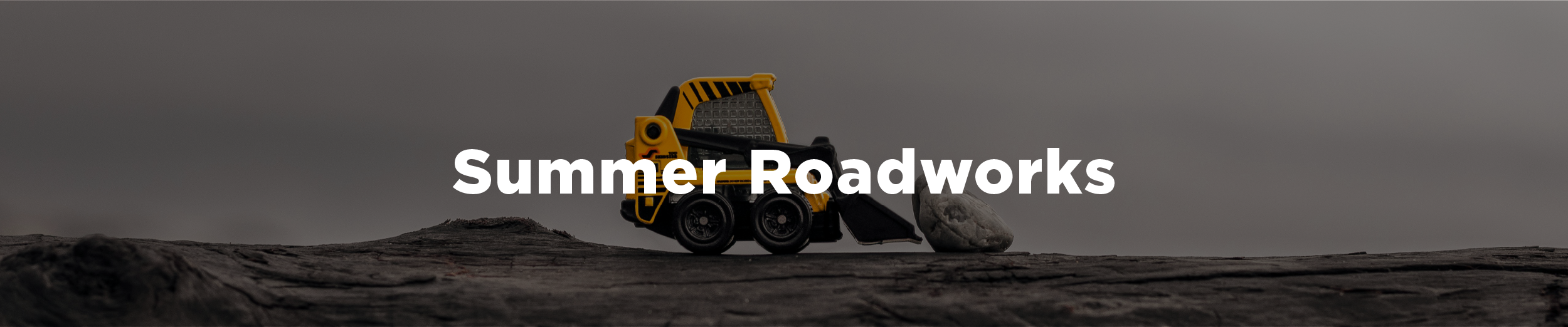 Forced perspective image of a toy bulldozer moving a rock with the overlaid text "Summer roadworks"