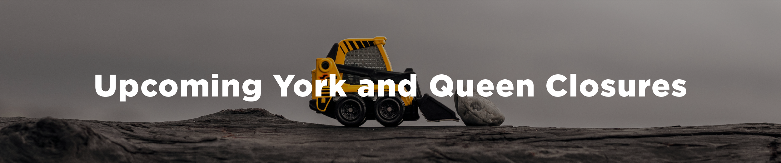 A small bulldozer toy trying to move a large rock with the overlaid text "Upcoming York and Queen Closures"