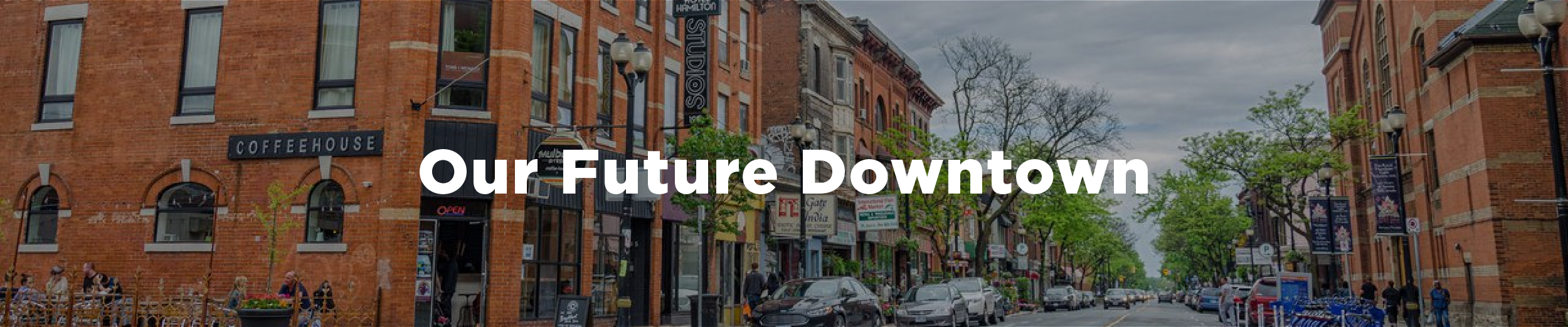 An image of downtown Hamilton at the corner of Mulberry and James with a series of midrise, mixed use buildings to the left and the Hamilton armoury on the right. The overlaid text reads "Our Future Dowtown"