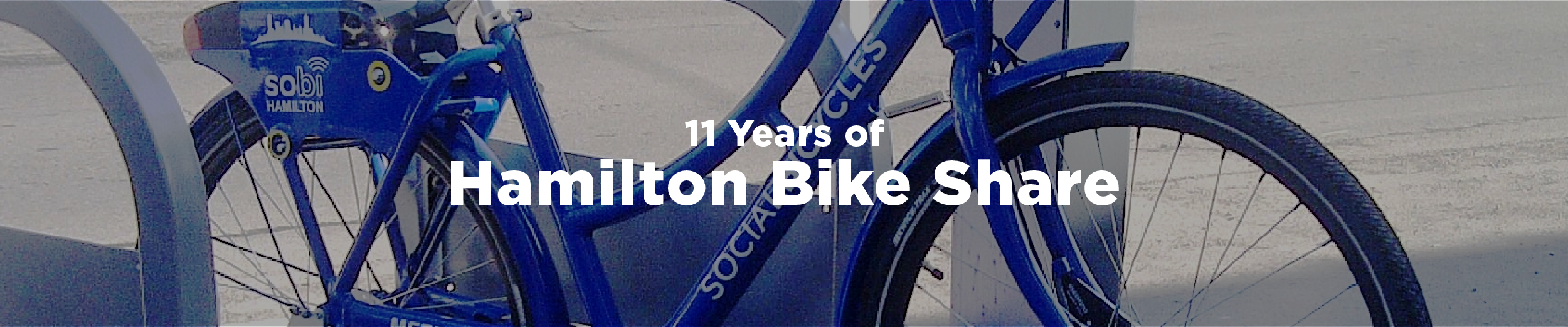 A blue Hamilton bike share bike at a docking station in the early spring with the overlaid text 11 Years of Hamilton Bike Share