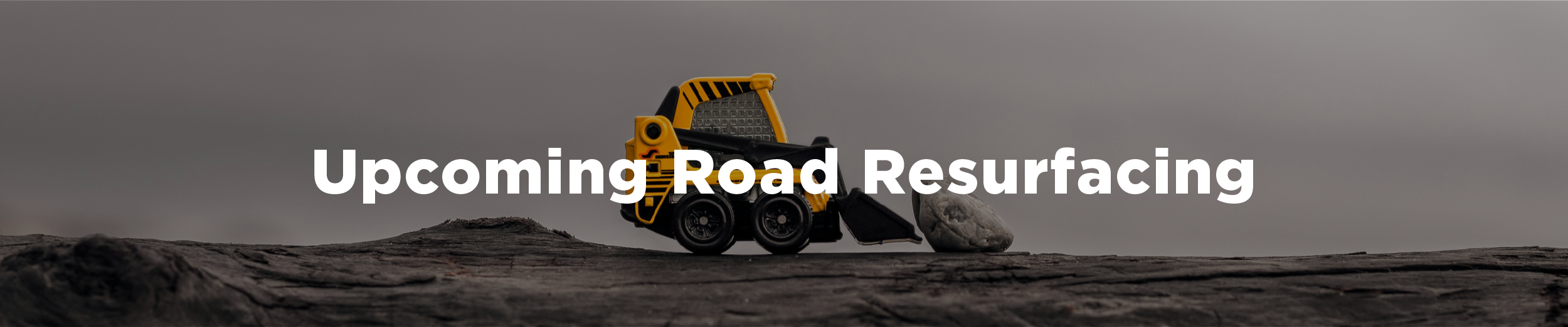Photo of a toy bulldozer pushing a large rock and the overlaid text "Upcoming road resurfacing"